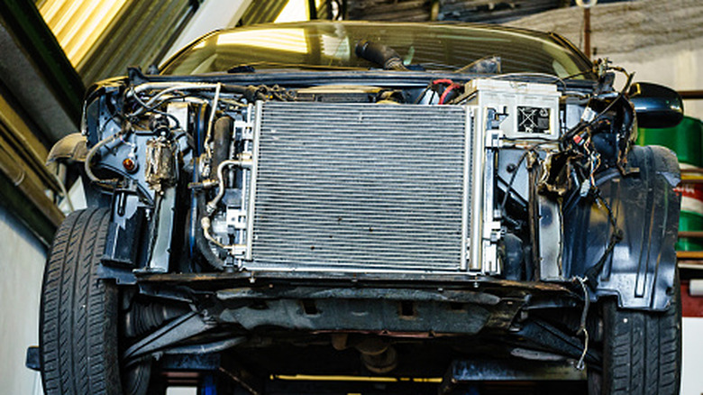A closer view of a car on a lift with no bumper or headlights to expose the radiator.
