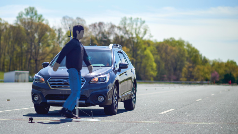 A testing dummy crosses a road in front of a vehicle.