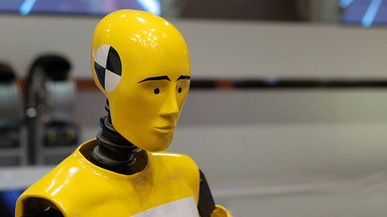 A yellow crash test dummy sits anxiously in a crash testing facility.