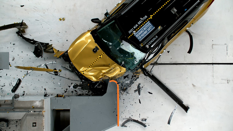 A yellow car is viewed from above after a front impact crash test with debris scattered.