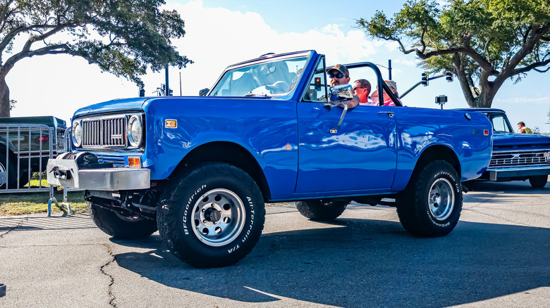 A blue open-top International Scout 80 with people inside of it