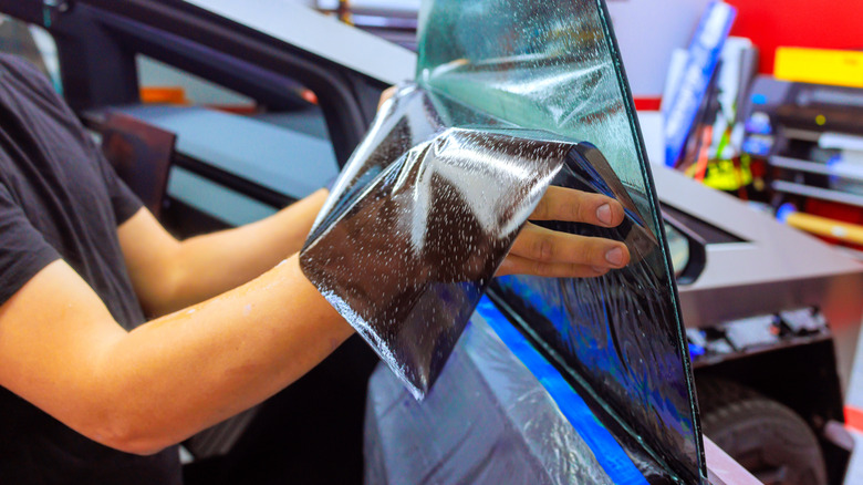 A professional window tint installer is applying window tint to the front right window of a Tesla Cybertruck.