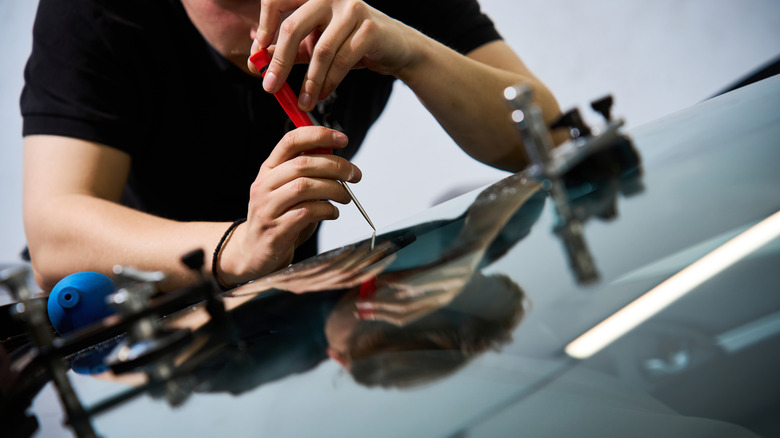 A person using a scriber to repair a damaged windshield.