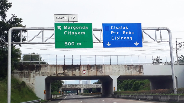 Blue and green signs above a highway in Clearview font