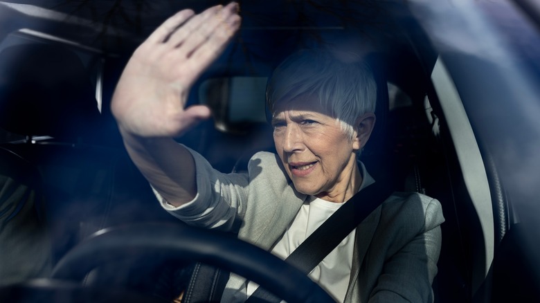 A white-haired woman driving at night holds her hand up to block light