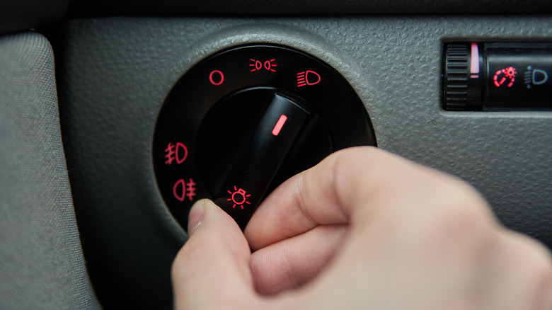 A man's hand reaches for a car's headlight rotary switch