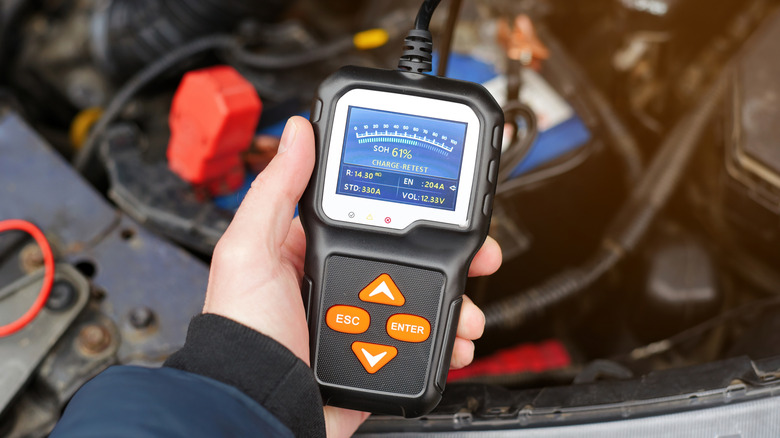 A technician holds a voltage tester above a car battery