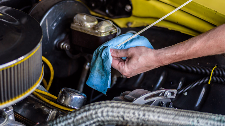 A person checking the oil level of a muscle car engine using the dipstick