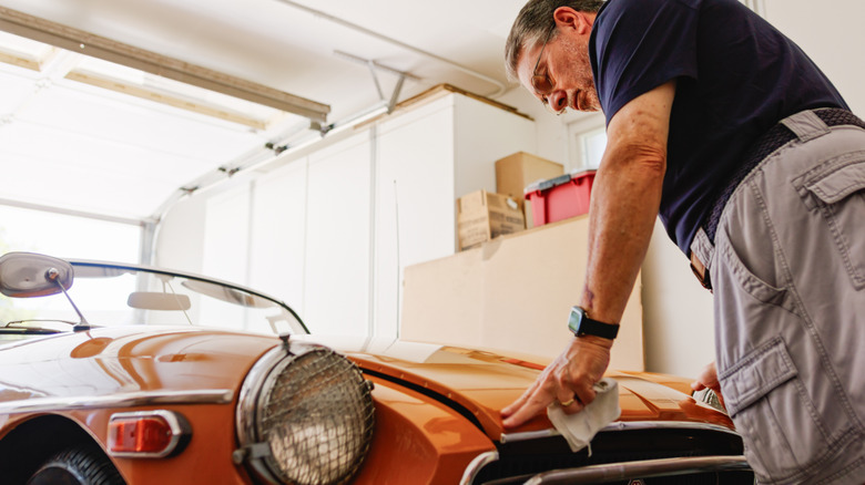 An elderly gentleman closing the hood of a classic car inside a garage