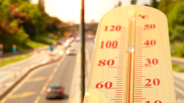 A thermometer showing hot ambient temperatures is set in front of a sun-drenched highway