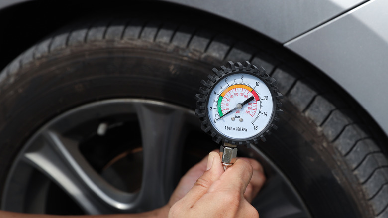 A man is using a tire pressure gauge to check the tire pressure of a car