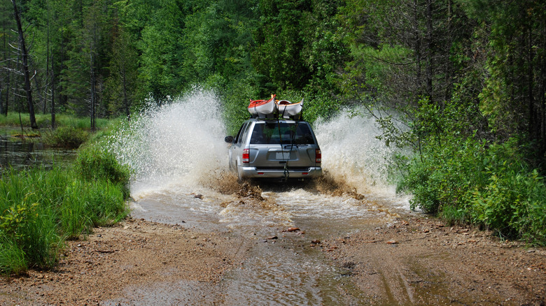 An SUV driving through water on a dirt road.