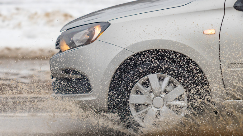The front of a car driving through a wet dirt road.