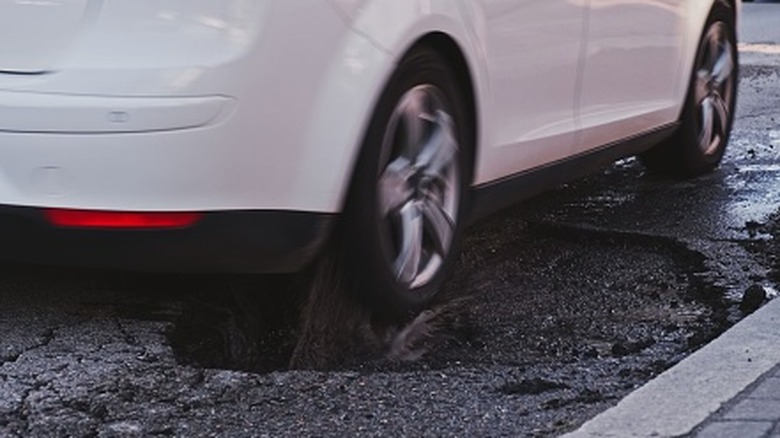 A vehicle driving over a pothole and pockmarked surfaces