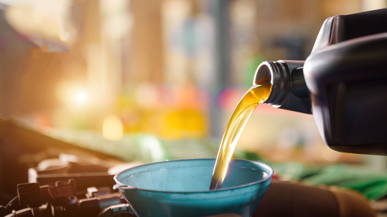 Fresh motor oil being poured through a funnel into the top of a car engine.