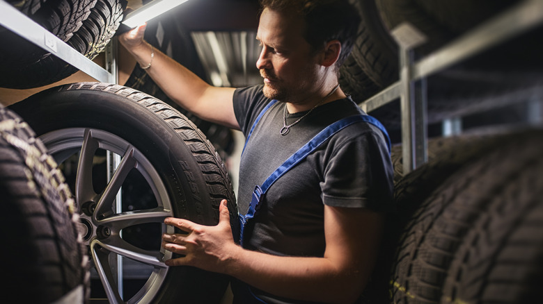 A man in overalls inspects tires in a garage-like space