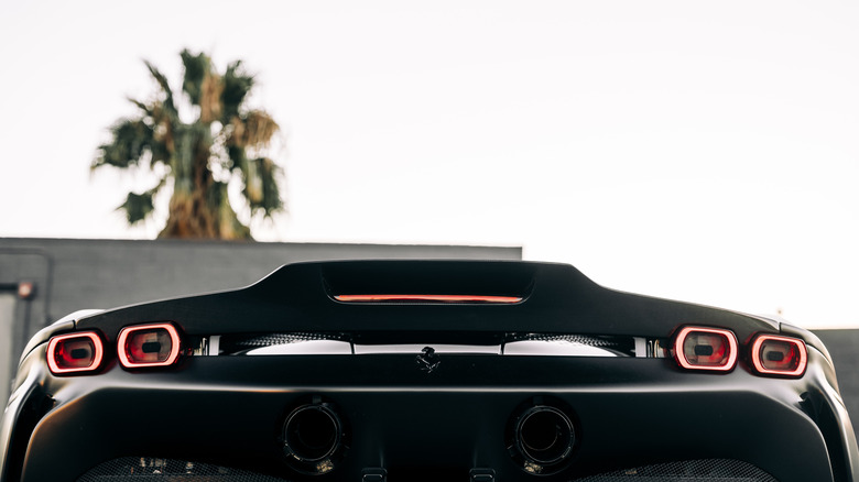 A rear-end close-up of a black Ferrari SF90 showcasing its wing, tail lights, exhaust, and third brake light.