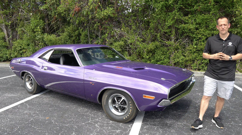 A guy stands next to a purple 1970 dodge challenger