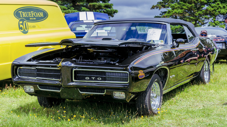 A black 1969 Pontiac GTO muscle car parked on grass at a car show