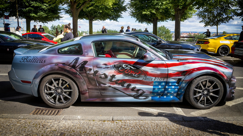 A side-profile view of a Ford Mustang with a U.S. flag graphic running along the side