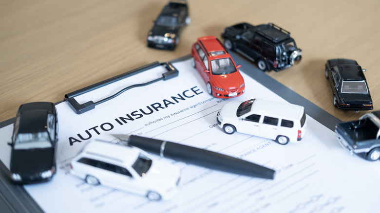 A car insurance form placed on a table with model cars and a pen on top of it.