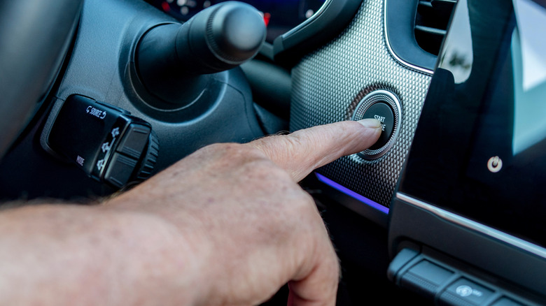 A driver's finger pressing the start button in a modern car