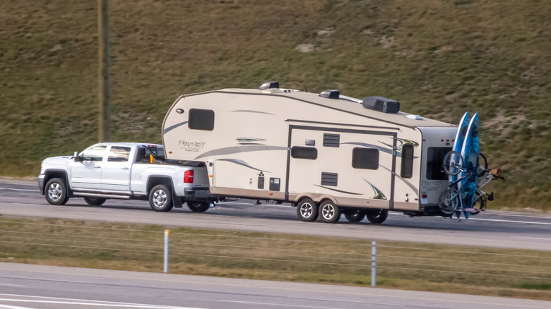 A white pickup truck towing a heavy camper trailer on the highway