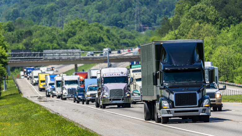 Photo of a black semi-truck leading a long line of heavy traffic.
