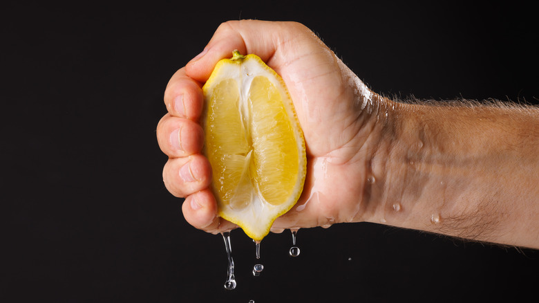 A hand squeezing a lemon, with juice dripping out