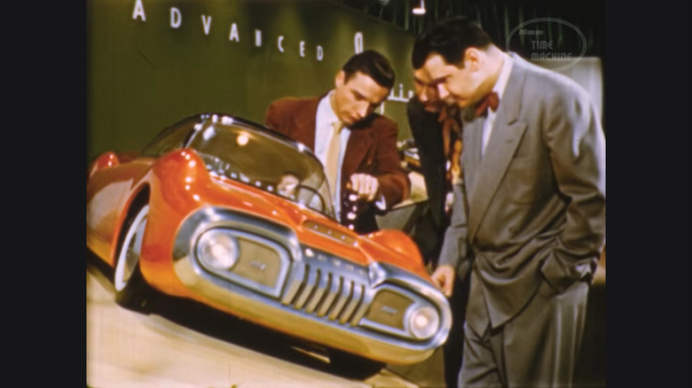 A group of Ford designers clad in suits check out an eclectic finished clay model of one of its designs on display in their studio.