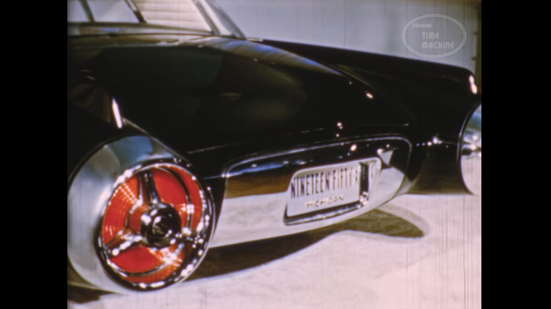 The rear tail end and lights of a finished Ford concept on a show floor display. The white Michigan license plate reads "nineteen fifty-x"
