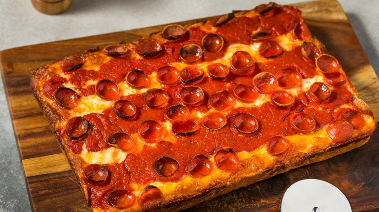 A detroit style pizza sitting connected a woody cutting board