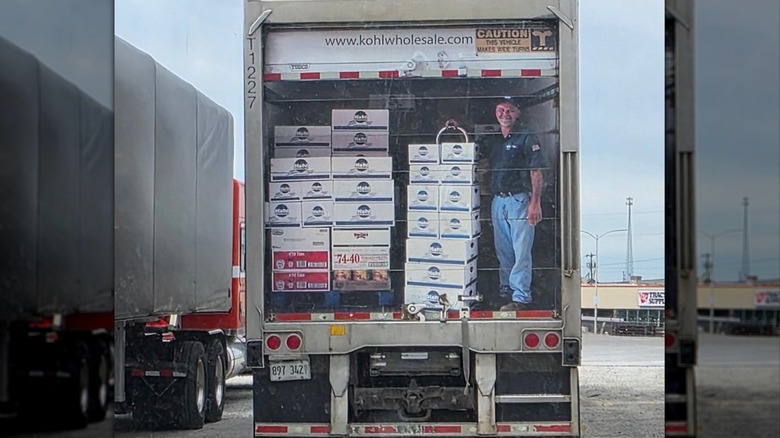 The back of a semi truck with a decal depicting a man standing inside with some boxes.