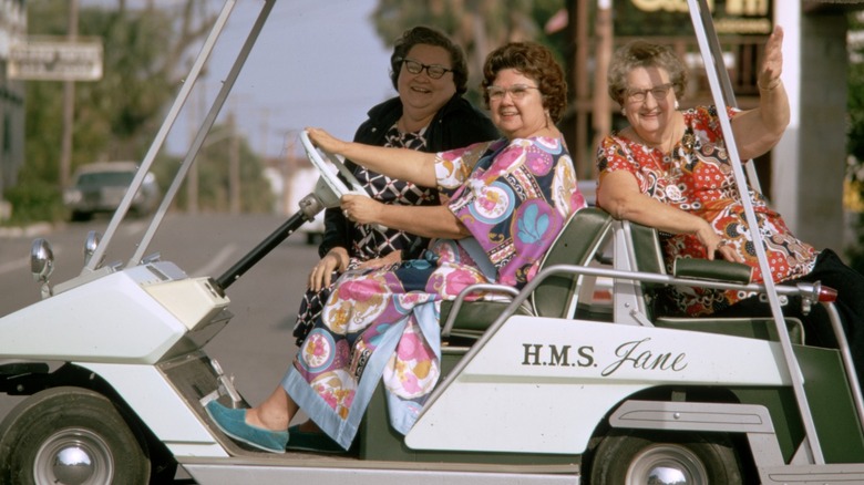 Three older women riding together in a white golf cart.