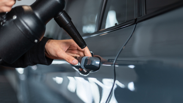 A professional detailer using a car dryer to dry a car's door handle