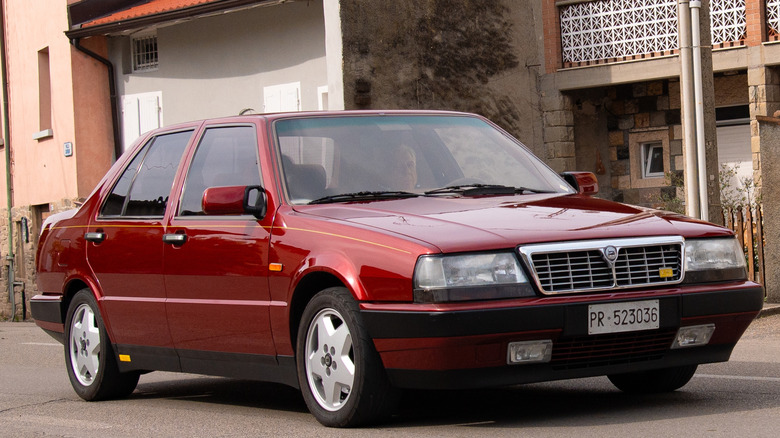 A Lancia Thema 8.32 in dark red parked next to a series of homes