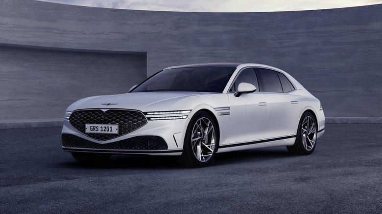 A white Genesis G90 outside near a modern structure.