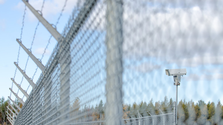 Surveillance camera at the airport surrounded by metallic fence and barbwire during autumn day
