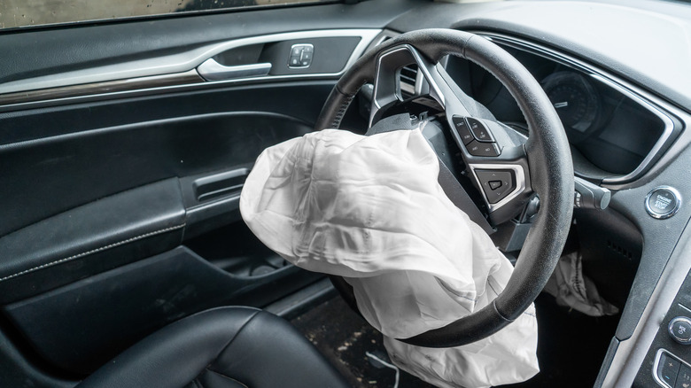 A car interior with an airbag deployed out of the steering wheel