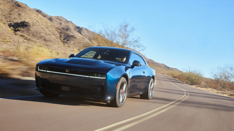 A dark blue 2024 Dodge Charger Daytona EV driving towards camera on a desert road.