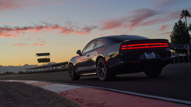 A 2024 Dodge Charger Daytona EV at sundown on a track corner, rear taillight illuminated.