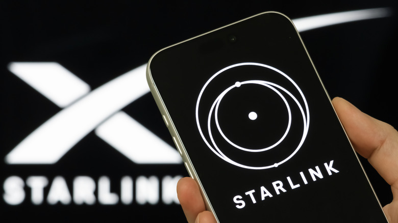A hand holding a phone with the Starlink app on the screen, with a Starlink logo in the background