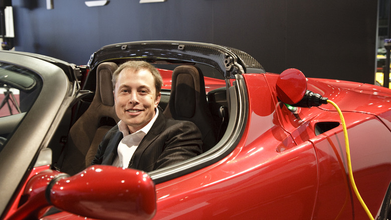 Elon Musk sitting in an original Tesla Roadster