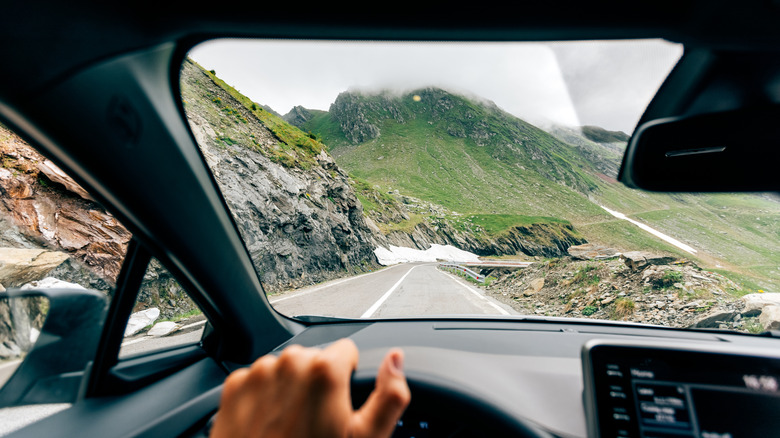 Looking out through the windshield while driving on a road toward a green mountain with mist.