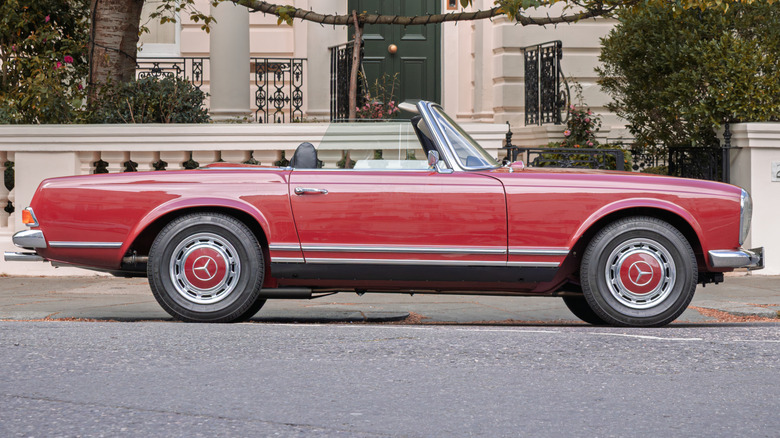 An old red Mercedes 280SL convertible parked in front of a stately home.