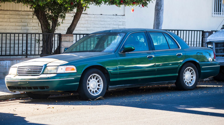 An old green Ford Crown Victoria parked on the side of the road.