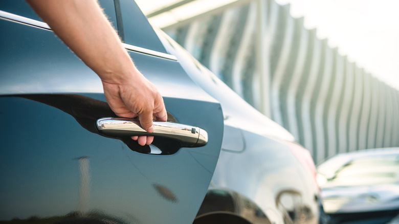 Close-up of a man's hand opening a car door with a building in the background.