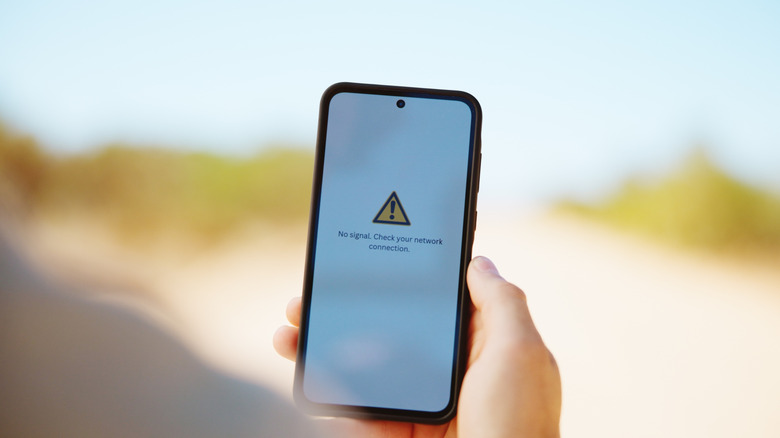 Person holds a phone with screen showing no service.