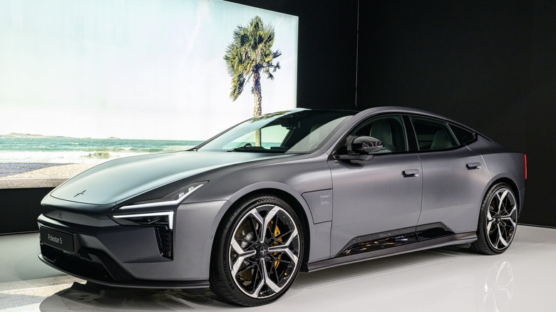 A gray Polestar parked in front a screen showing a tropical landscape