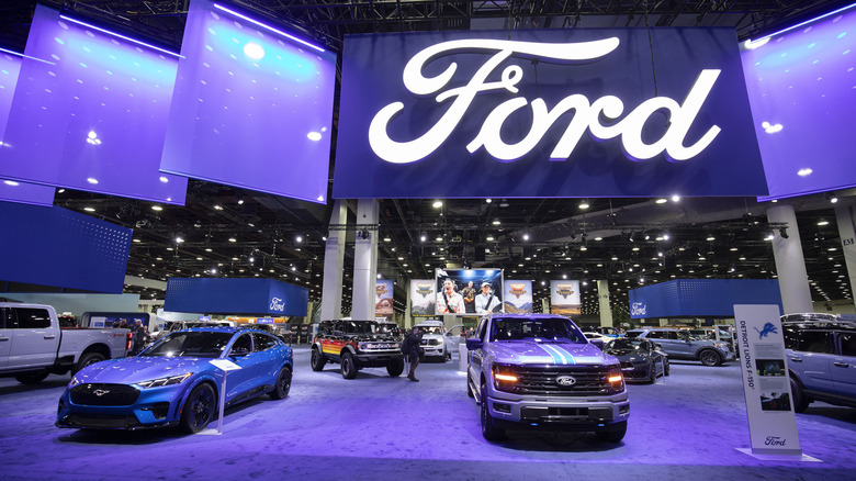 the ford booth at the 2025 NAIAS featuring a Ford F-150 and a Ford Mustang Mache-e parked beneath a huge FORD banner
